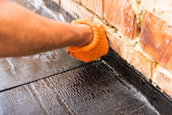 A man coats a roof while wearing orange gloves