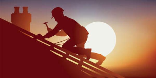 A man works on a roof as the sun sets behind him