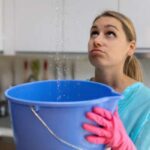 A woman holds a bucket to capture water from the leaking section of her roof