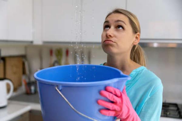 A woman holds a bucket to capture water from the leaking section of her roof